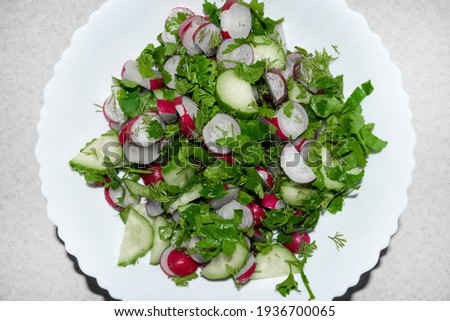 Salad with radish, dill, parsley, fresh cucumbers and oil in big white bowl