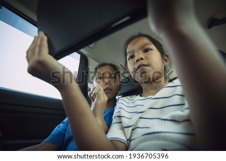 Two asian child girls sitting on backseat and watching cartoon in tablet together while traveling in the car with fun. Childhood and family lifestyles in car concept.
