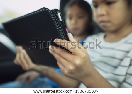 Two asian child girls sitting on backseat and watching cartoon in tablet together while traveling in the car with fun. Childhood and family lifestyles in car concept.