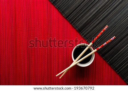 Chopsticks and bowl with soy sauce on bamboo mat