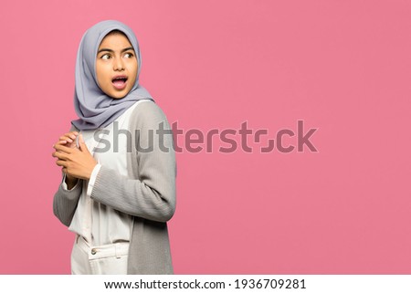 Portrait of shocked young Asian woman looking aside with folding raised hand