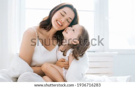 A nice girl and her mother enjoy sunny morning. Good time at home. Child wakes up from sleep. Family playing on the bed in the bedroom.   