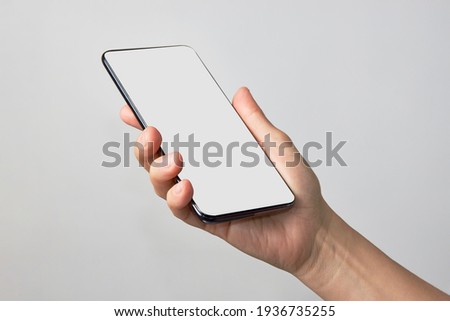 Woman hand holding phone on white background with copy space. Woman holding smartphone with white screen. Hand with blank cellphone display, close-up Royalty-Free Stock Photo #1936735255