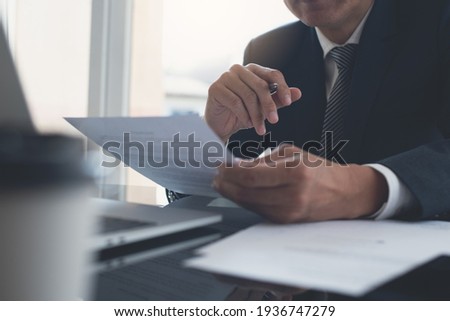 Signing contract, business agreement and deal concept. Closeup businessman reading business contract documents at desk with laptop computer, busy with paperwork. Man manager proofing report at office Royalty-Free Stock Photo #1936747279