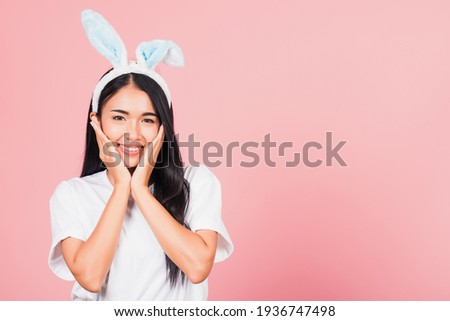 Happy Easter Day. Beautiful young woman teen smiling wearing Easter rabbit bunny ears holding her cheeks excited surprised, Portrait female face touch massage, studio shot isolated on pink background