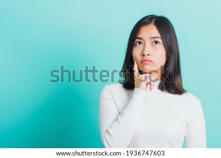 Young beautiful Asian woman hand near the face and thinking, Portrait  female touch chin dream dreamy having doubts, studio shot isolated on a blue background Royalty-Free Stock Photo #1936747603
