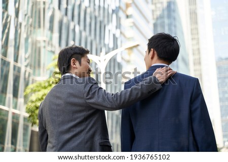 asian corporate executive giving subordinate a pat on the back while walking in street of central business district of modern city Royalty-Free Stock Photo #1936765102