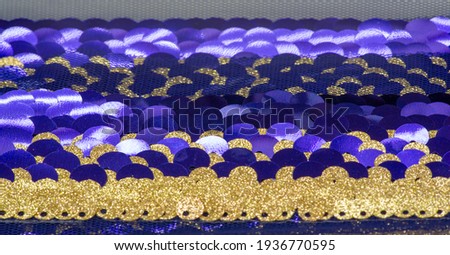 Sequins in blue, gold. Ribbon for fabric decoration. Background texture, sunrise. Smooth slope of rows of round blue, gold sequins on a thin mesh of fabric.