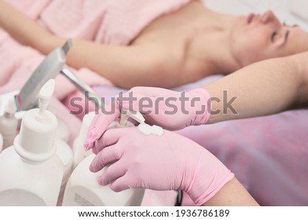 Closeup photo of professional beautician in medical gloves applying antiseptic cream on hands before procedure