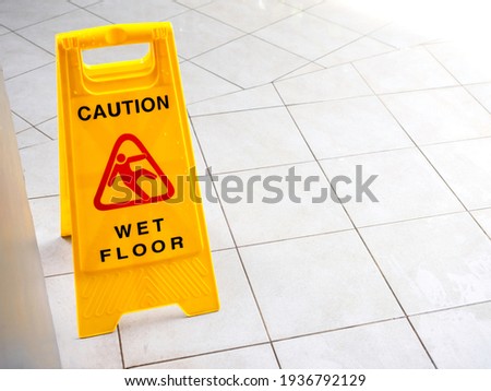 Wet floor caution sign on walkway near the building after raining. Warning yellow plastic caution wet floor sign on the ground with copy space.