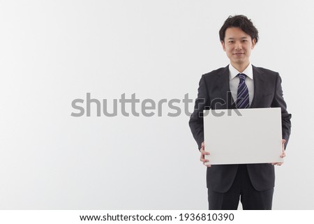 A young businessman in a suit stands with a smile and holds a white notebook.