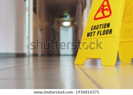 Yellow sign of slippery floor in the room after cleaning. A sign that reads Caution is a long empty industrial corridor.