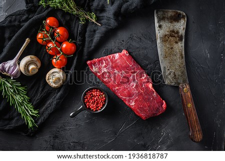 Raw, flap or flank, also known Bavette steak near butcher knife with pink pepper and rosemary. Black background. Top view. Royalty-Free Stock Photo #1936818787