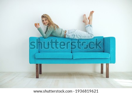 Beautiful woman is drinking tea on the sofa at home. Sportive young girl doing yoga pose on the couch. High quality photo.