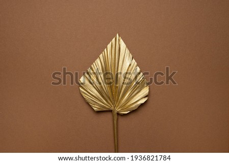 Gold colored tropical palm leaves on beige background flat lay top view copy space. Creative summer background with tropical leaves. Golden background, minimal nature concept