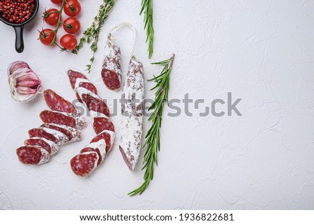 Dry cured fuet salami sausage slices with herbs on white surface, top view with copy space.