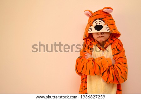 The child is sad, annoyed, offended and displeased in pajamas, in a tiger kigurumi costume. Children's problems in the family, with parents, with friends.  Upbringing problems, lack of understanding
