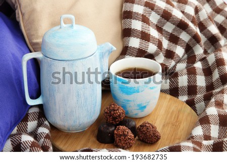 Cup and teapot with candies on wooden stand on bed close up