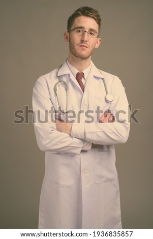 Young handsome man doctor wearing eyeglasses against gray background