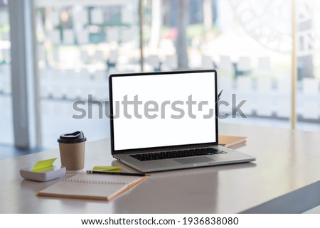 Blank white screen of a laptop and a notebook placed on the table at the office. Mock up. Royalty-Free Stock Photo #1936838080