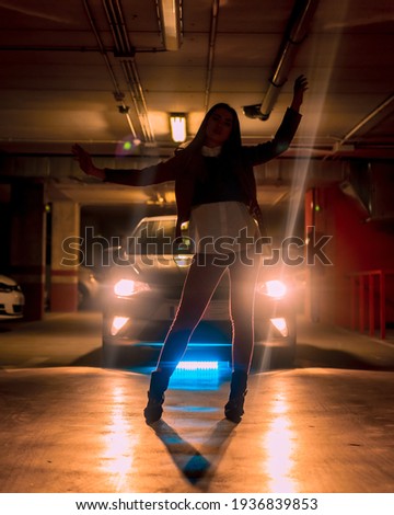 Photography with blue neon signs in front of a car in a parking lot. Portrait of a young pretty blond Caucasian woman in silhouette