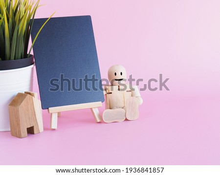 A blackboard for writing your text with the wooden doll and house, tree on a bright pink backdrop
