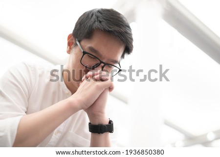 An Asian man praying on a bench in a Christian church.