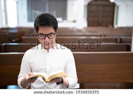 Asian man is reading the Holy Bible and praying in a worship room in a Christian church.