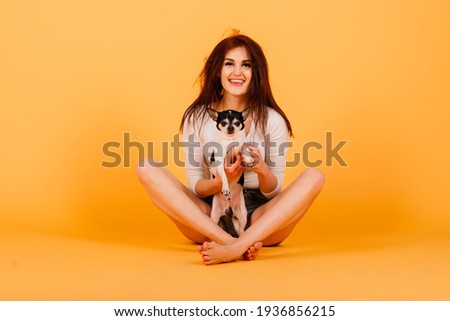 Beautiful young woman holding her dog on a yellow background.