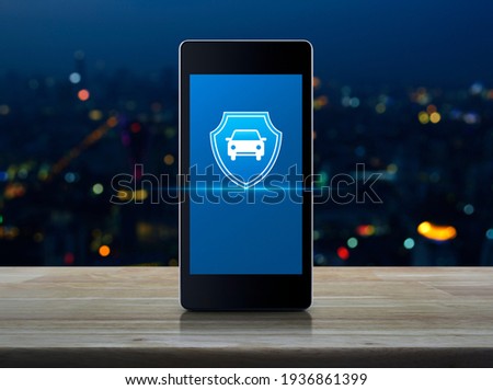 Car with shield flat icon on modern smart mobile phone screen on wooden table over blur colorful night light city tower and skyscraper, Business automobile insurance online concept