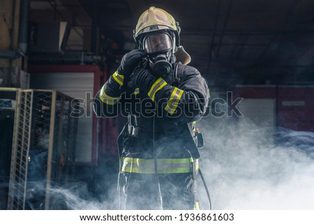 Portrait of a fireman wearing firefighter turnouts and helmet. Dark background with smoke and blue light. Royalty-Free Stock Photo #1936861603