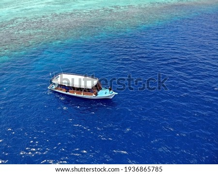 Aerial picture of man standing front of a single white diving boat on turquoise water and Maldivian coral reef. Picturesque scenery. Scuba diving day trip.