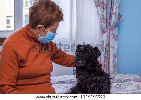 senior woman with her dog at home and wearing a medical mask in times of pandemic