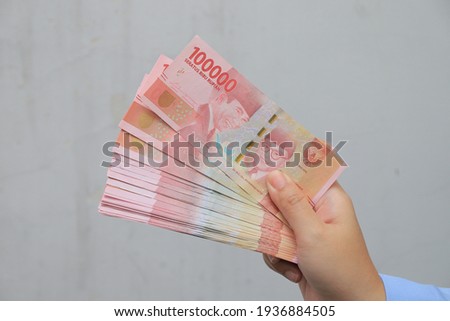 woman's hand showing rupiah banknotes on white background. IDR 100000. Royalty-Free Stock Photo #1936884505