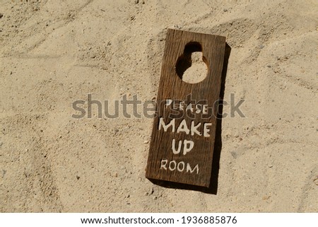 Sign for hanging in front of the hotel room "Please Make Up Room" placed on the sand.
