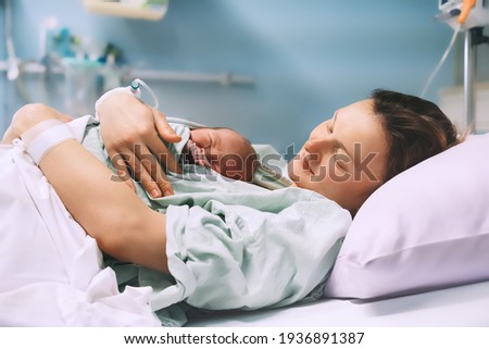 Mother and newborn. Child birth in maternity hospital. Young mom hugging her newborn baby after delivery. Woman giving birth. First moments of baby life after labor. Royalty-Free Stock Photo #1936891387