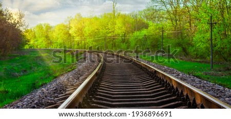 Morning landscape on the railway tracks. The sun's rays are the green grass and the rails on which the train travels. Trees along the railway. Royalty-Free Stock Photo #1936896691