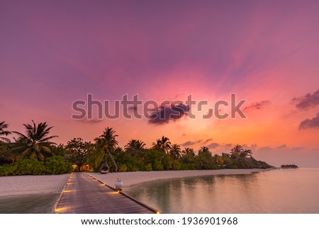 Sunset on Maldives island, luxury resort hotel and wooden pier jetty. Wonderful colorful sky clouds and beach sea horizon. Summer romantic vacation holiday, travel concept. Paradise sunset landscape
