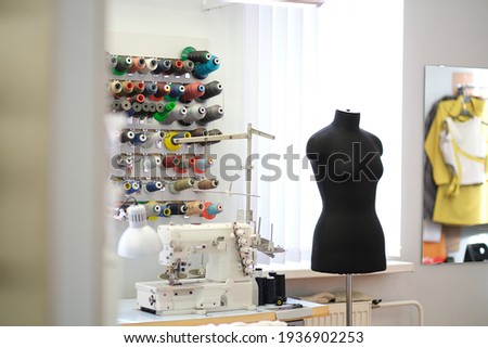 Shot of seamstress workplace. Fashion Design Studio. Sewing Machine and Various Sewing Related Items on the Table, Mannequins Standing, Colorful Fabrics.