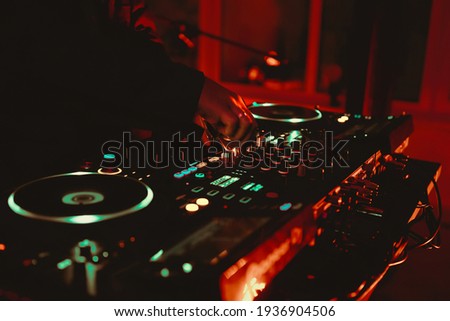 Dj playing music on rave party in nightclub.Professional disc jockey plays concert turntables,sound mixer devices on stage in dark night club.Royalty free curated collection with parties and concerts Royalty-Free Stock Photo #1936904506