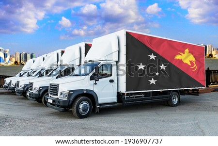Papua New Guinea flag on the back of Five new white trucks against the backdrop of the river and the city. Truck, transport, freight transport. Freight and Logistics Concept