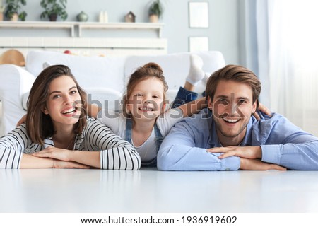 Young Caucasian family with small daughter pose relax on floor in living room, smiling little girl kid hug embrace parents, show love and gratitude, rest at home together Royalty-Free Stock Photo #1936919602