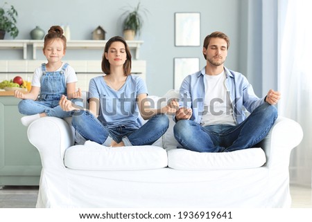 Calm young family with little daughter sit on couch practice yoga together, happy parents with small preschooler girl child rest on sofa meditate relieve negative emotions on weekend at home Royalty-Free Stock Photo #1936919641