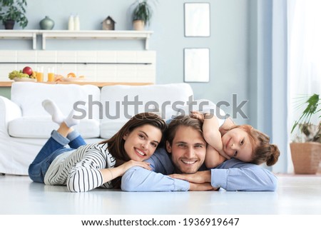 Young Caucasian family with small daughter pose relax on floor in living room, smiling little girl kid hug embrace parents, show love and gratitude, rest at home together Royalty-Free Stock Photo #1936919647