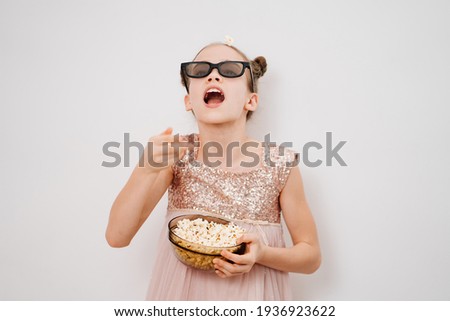 A teen girl with glasses to watch 3D movies throws in his mouth popcorn stands against a white wall. Home or online cinema. harmful snacking.