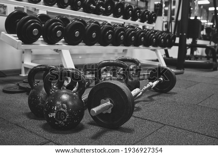 Dumbbells and kettlebells on a floor. Bodybuilding equipment. Fitness or bodybuilding concept background. black and white photography Royalty-Free Stock Photo #1936927354