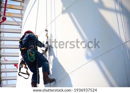 The worker ascended high with ropes to measure the thickness of the storage tank.