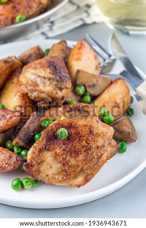 Chicken stew with potatoes, mushrooms and green peas, on a white plate and in a metal pot, vertical, closeup