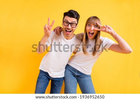 Photo of funny adorable two persons dressed white t-shirt glasses dancing showing v-sign cover eye isolated yellow color background