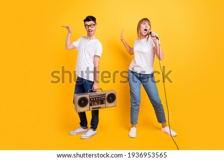 Photo of pretty young couple wear white t-shirt spectacles holding boombox singing mic dancing isolated yellow color background